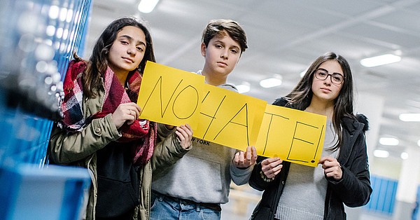Über klicksafe Das Bild zeigt zwei Mädchen und einen Jungen, die ein gelbes Poster halten mit Aufschrift "NOHATE!"